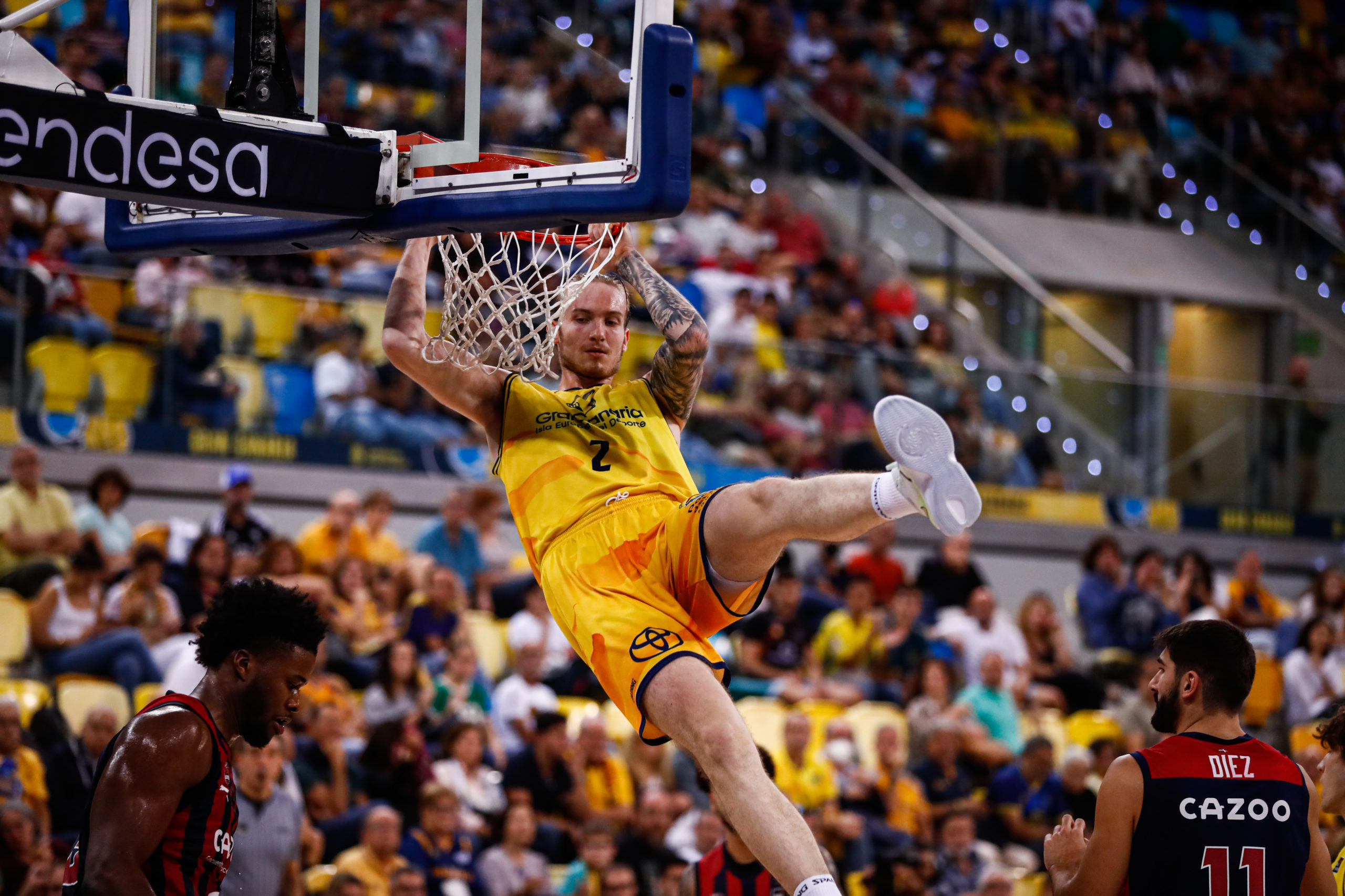 Jugador del Gran Canaria encesta con un mate frente a oponentes en un partido de baloncesto.