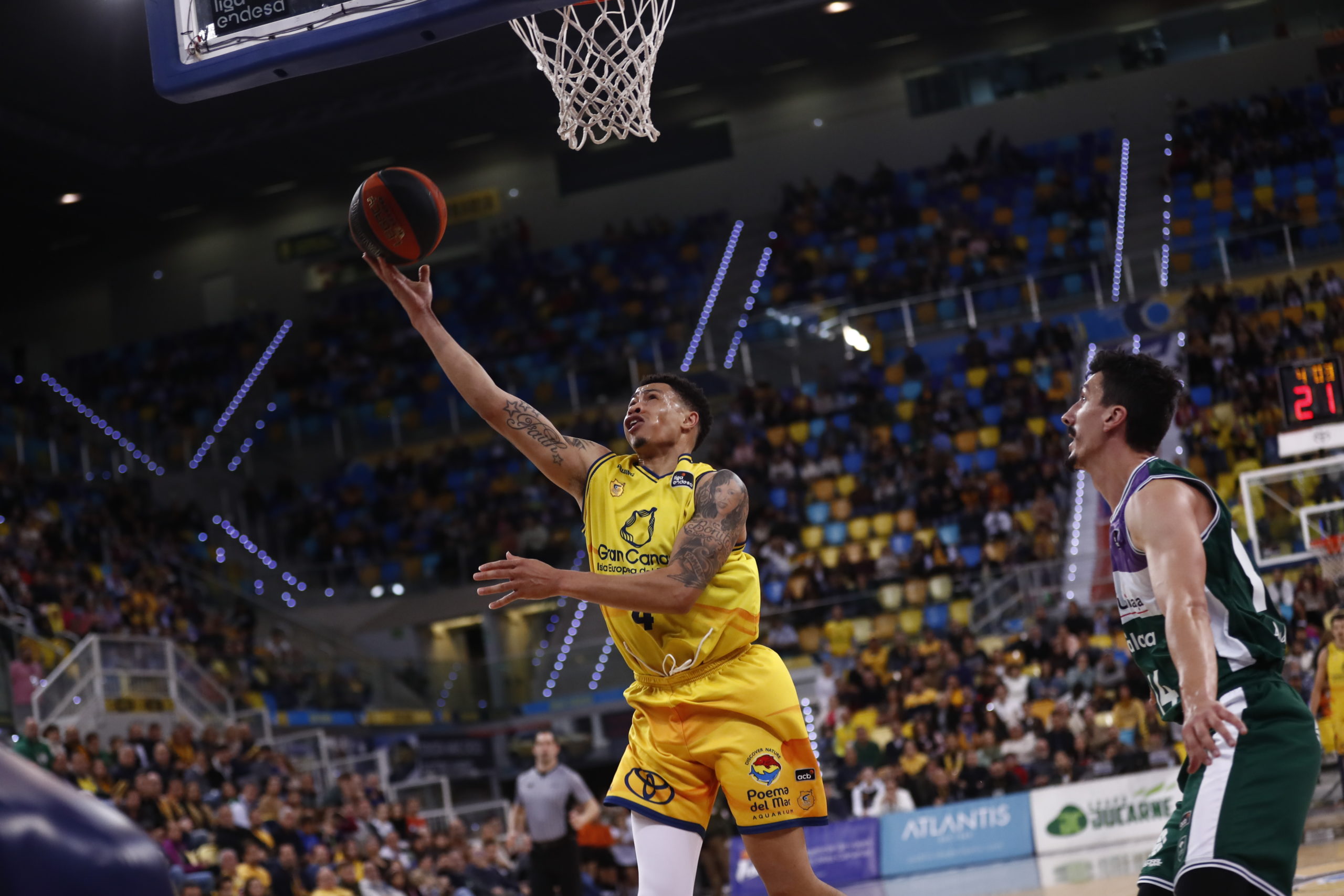 Jugador del Gran Canaria lanza a canasta mientras un rival de Unicaja lo defiende.