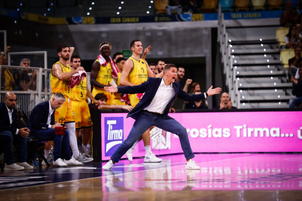 Entrenador gesticula enérgicamente mientras el equipo observa desde el banquillo.