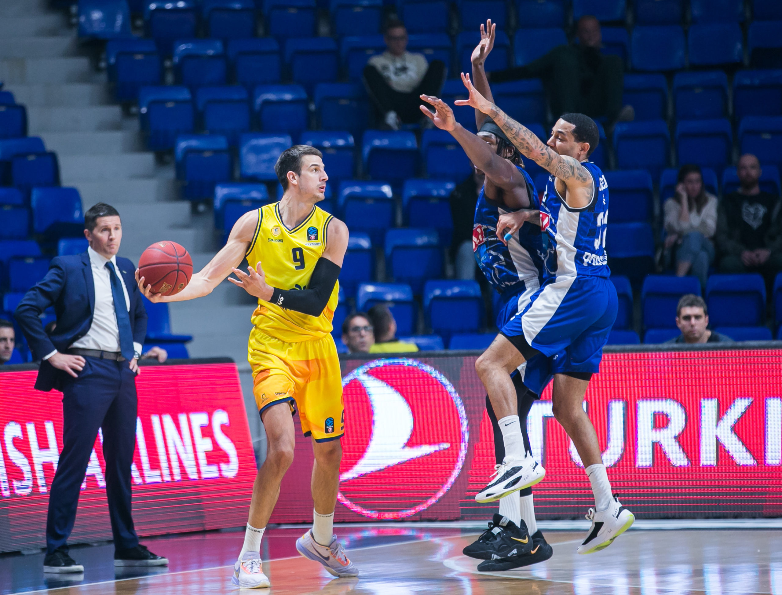 Jugadores de baloncesto en acción durante un partido, uno lanzando y otros defendiendo.