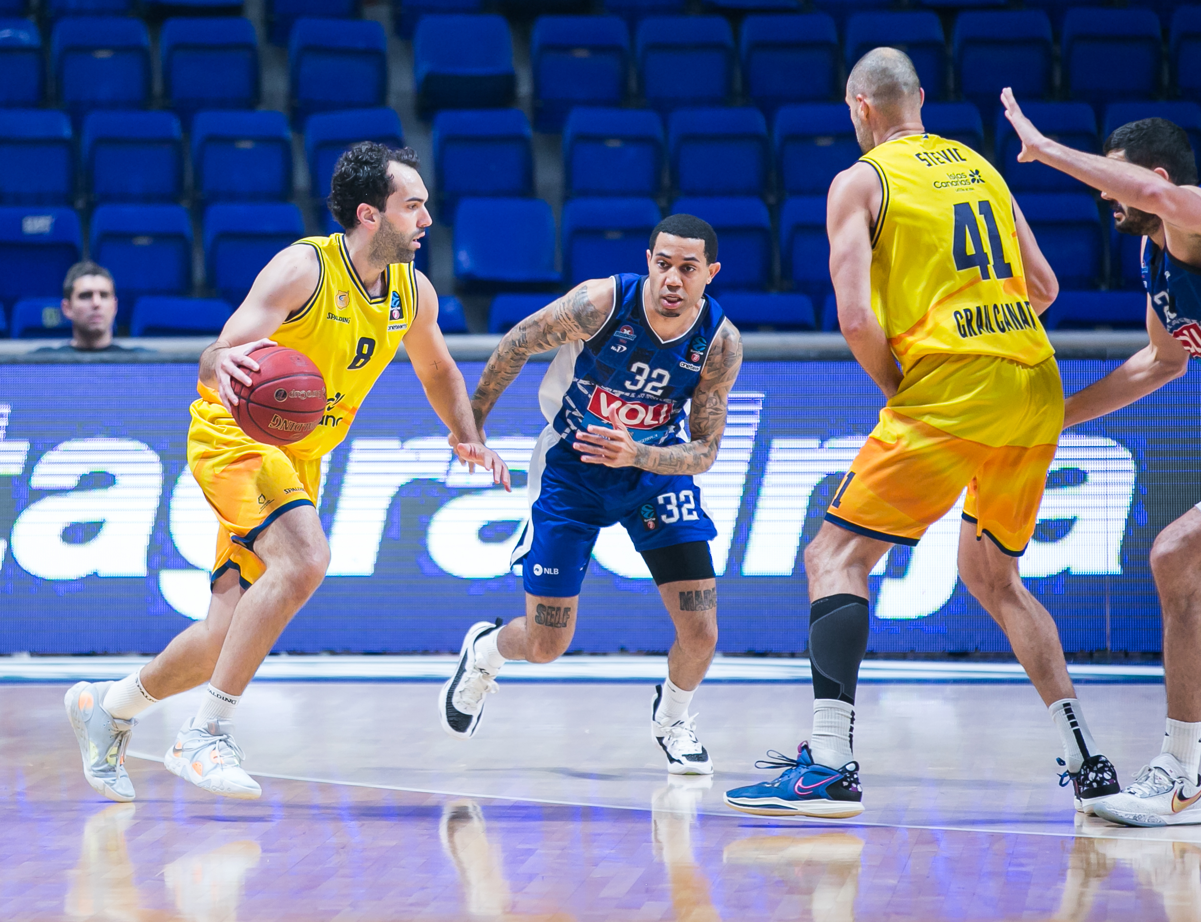 Jugadores en acción durante un partido de baloncesto, con un jugador driblando.