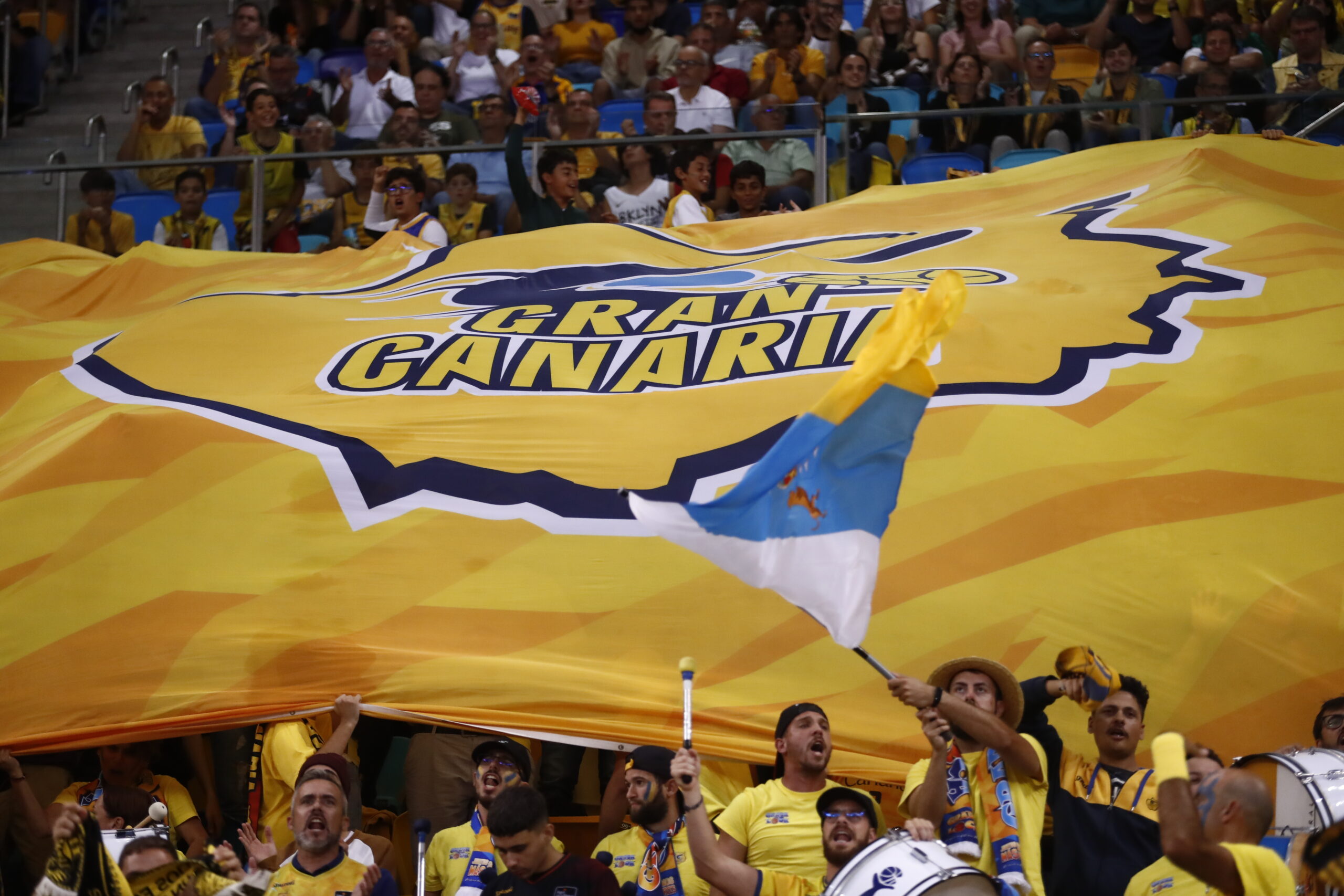 Aficionados del Club Baloncesto Gran Canaria sosteniendo una gran bandera amarilla.