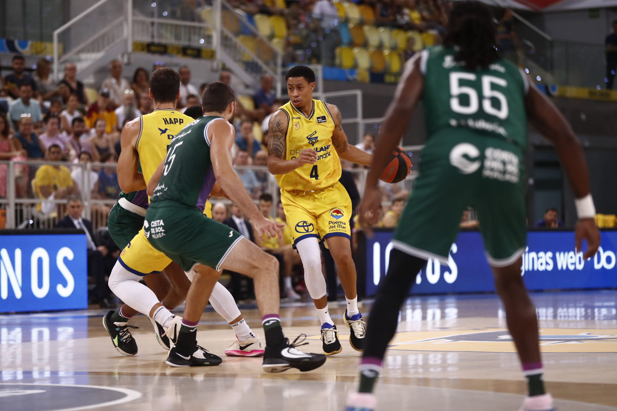 Jugador con balón en un partido de baloncesto, rodeado por defensores.