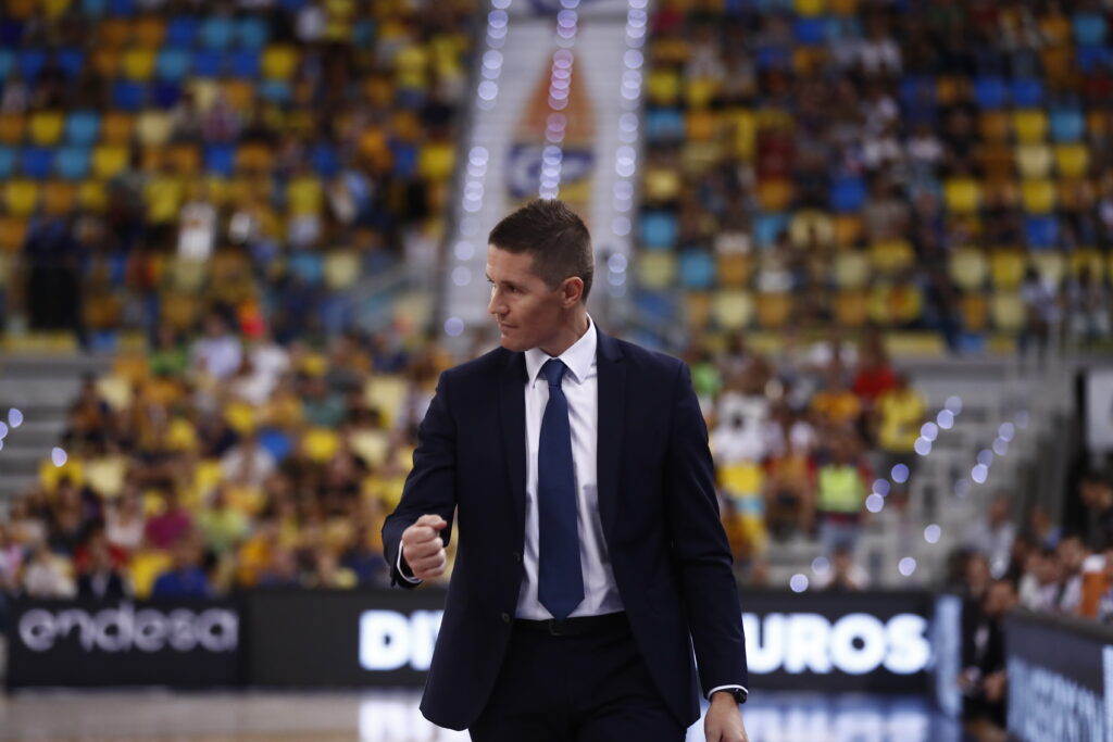 Entrenador Jaka Lakovic caminando por la pista durante un partido, con público al fondo.