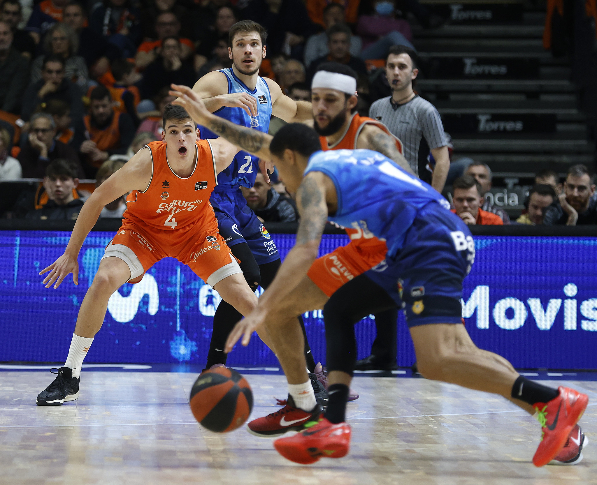 Jugadores de baloncesto en acción durante un partido, con un balón en juego.