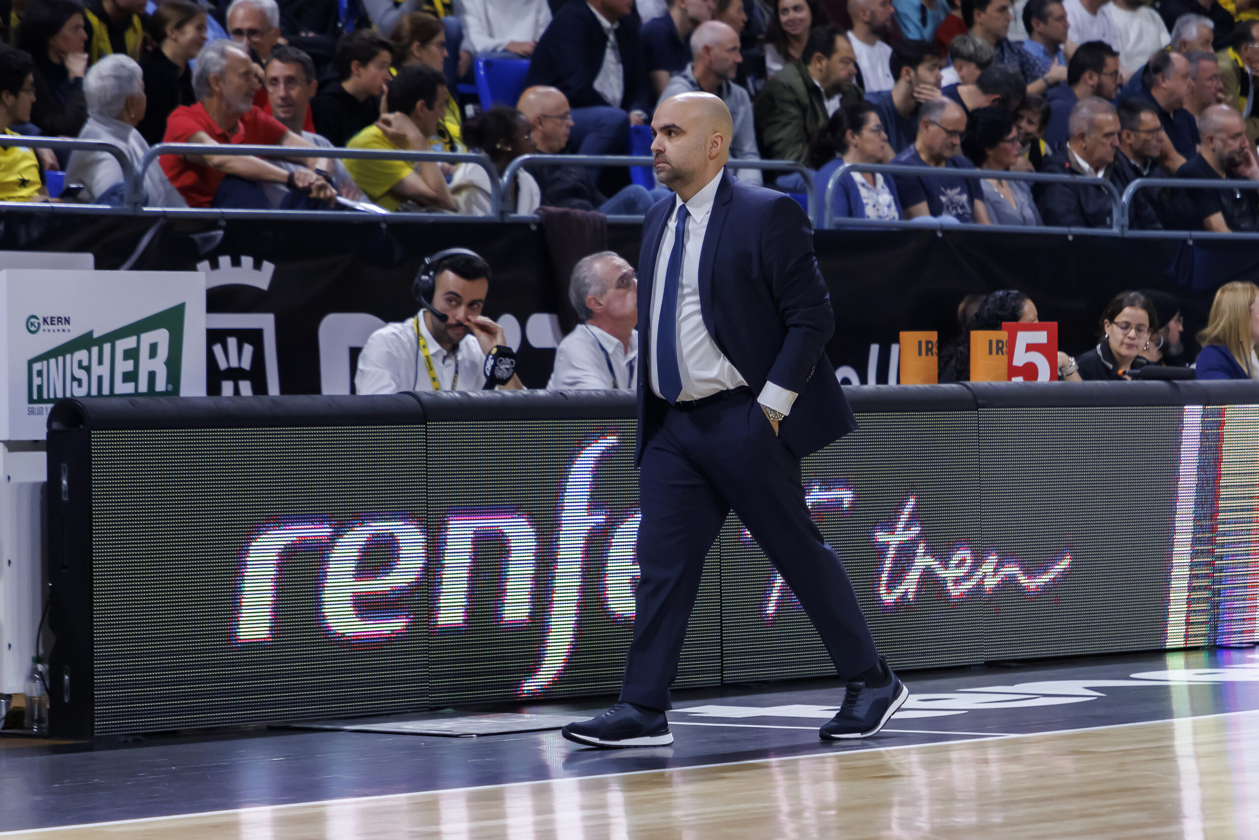 Entrenador caminando por la cancha durante un partido, observando el juego.