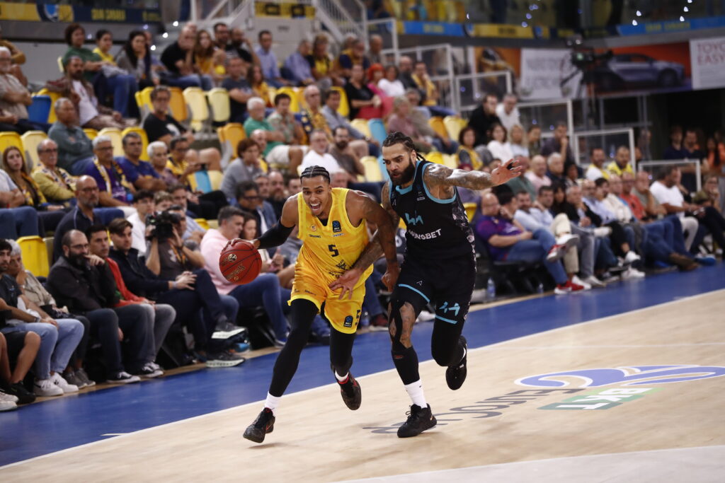 Jugador del Gran Canaria driblando mientras es seguido por un oponente en un partido.