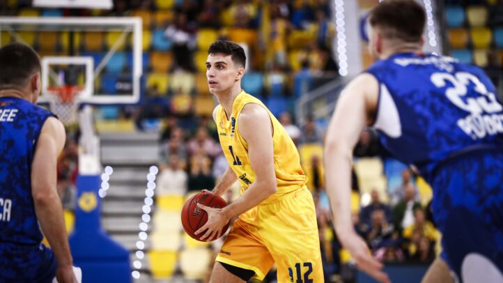 Jugador de baloncesto en acción con balón en una cancha, rodeado de adversarios.