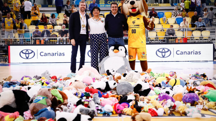 Tres personas posan junto a una gran cantidad de peluches en la pista de baloncesto.