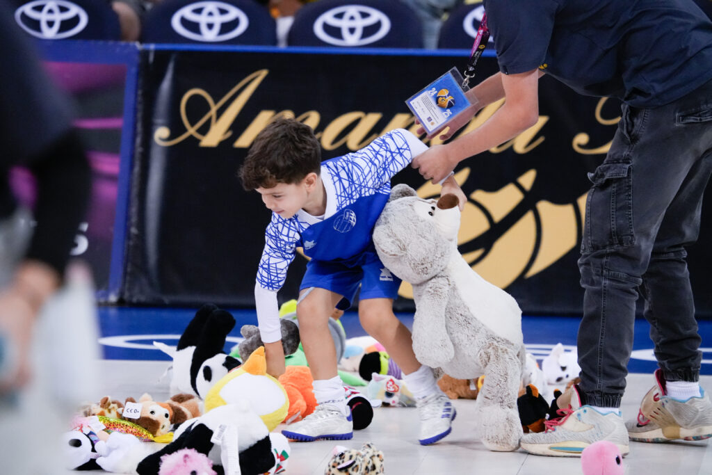 Niño recogiendo peluches en una cancha con fondo del Club Baloncesto Gran Canaria.