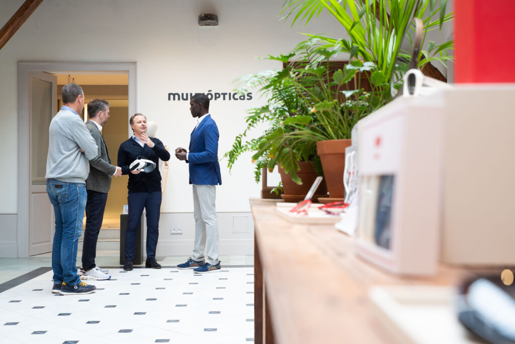 Cuatro personas conversan en una tienda de multiópticas, rodeadas de plantas.