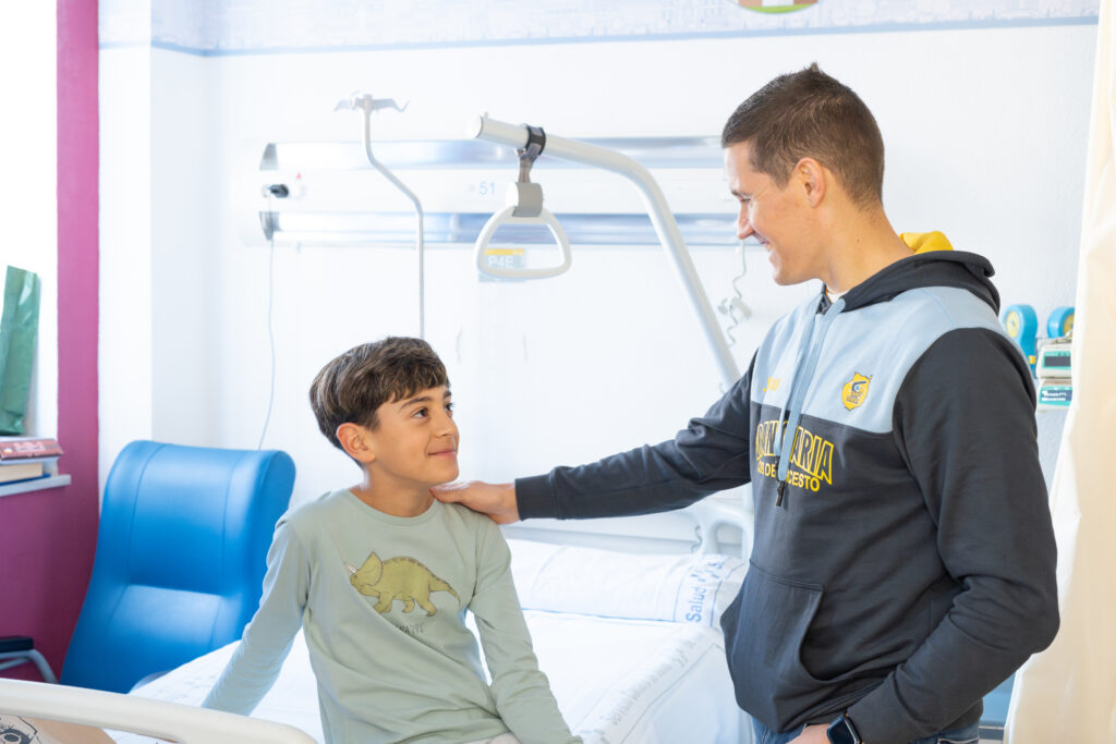 Visitante del Dreamland Gran Canaria sonríe y conversa con un niño en un hospital.