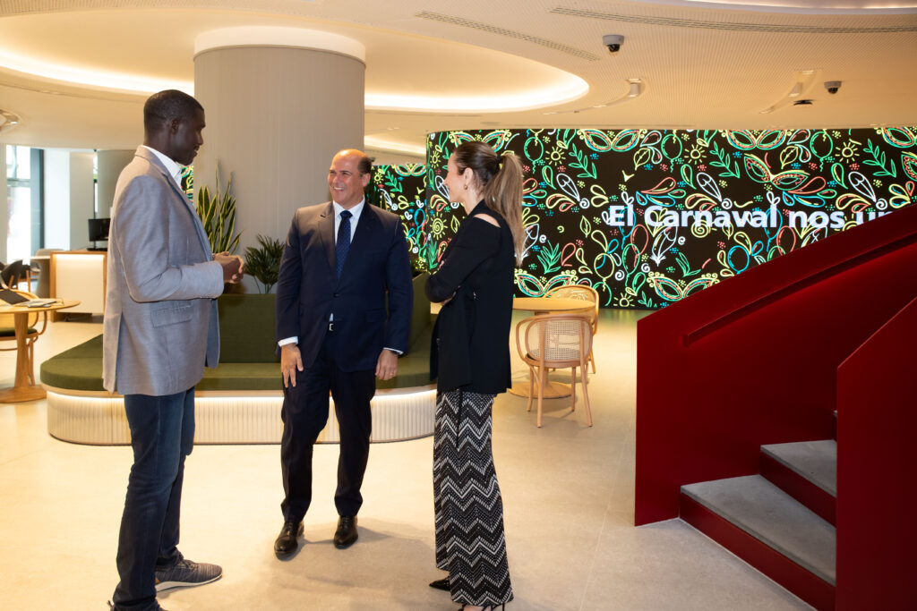 Tres personas conversan en un ambiente moderno; fondo con decoraciones coloridas.