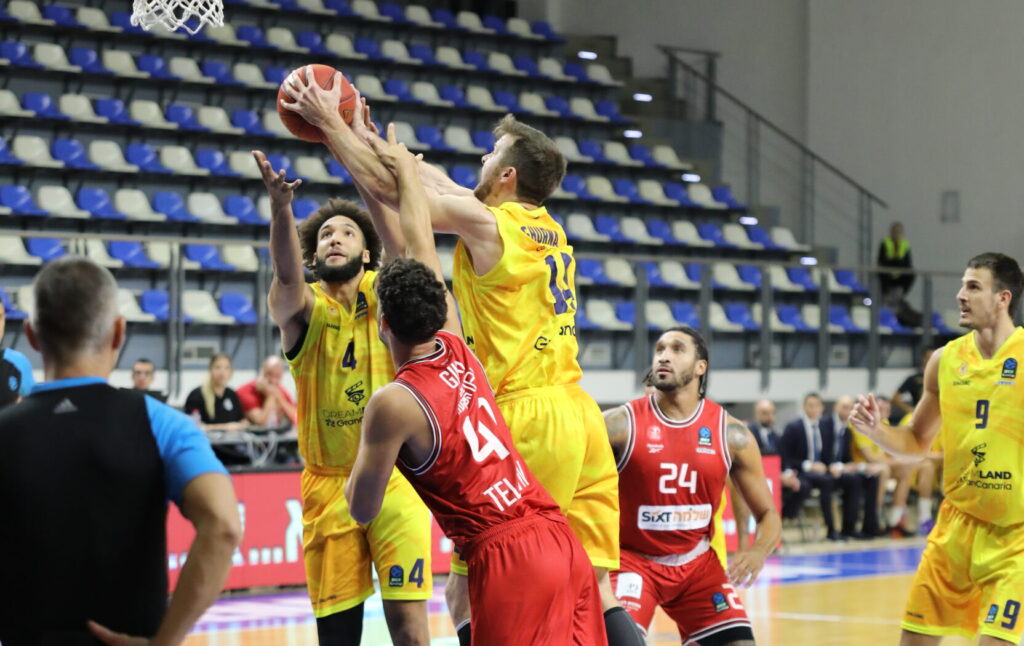 Jugadores de baloncesto en acción durante un partido, uno lanzando a canasta.