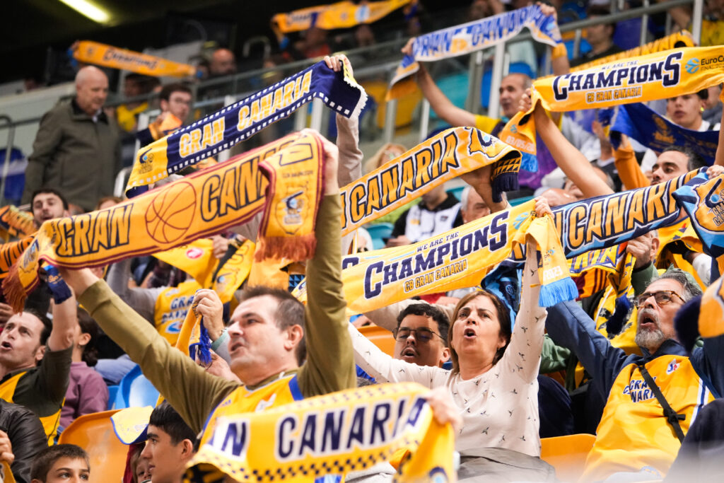 Aficionados del Gran Canaria animando con bufandas en un partido de baloncesto.