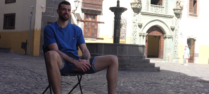 todos los días""","Pierre Pelos sentado en una silla en una plaza pintoresca, sonriendo.