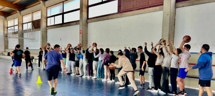Grupo de jóvenes practicando baloncesto en un gimnasio bajo la supervisión de entrenadores.
