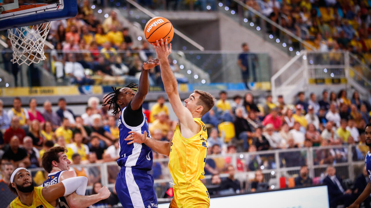 Juego intenso entre dos equipos de baloncesto en un estadio lleno de espectadores.