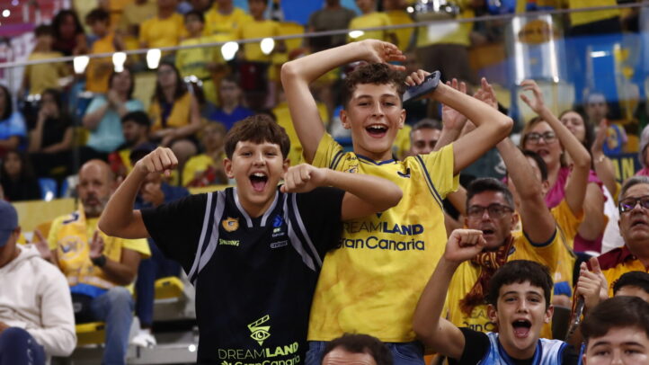 Niños animando en un partido, con público de fondo vestido de amarillo.