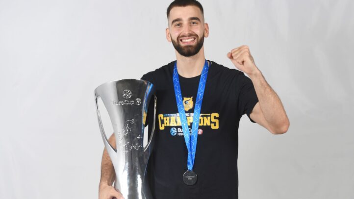 Jugador sonriente sosteniendo un trofeo y medalla, celebrando un logro deportivo.