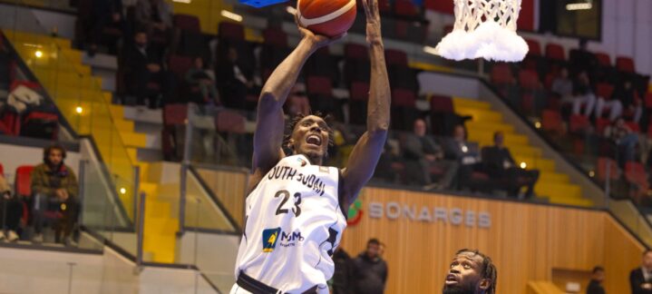 con dos representantes del Dreamland Gran Canaria","Jugador de baloncesto realizando una canasta bajo el aro, con dos defensores atentos.