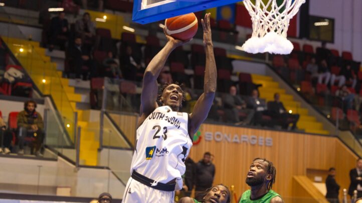 con dos representantes del Dreamland Gran Canaria","Jugador de baloncesto realizando una canasta bajo el aro, con dos defensores atentos.