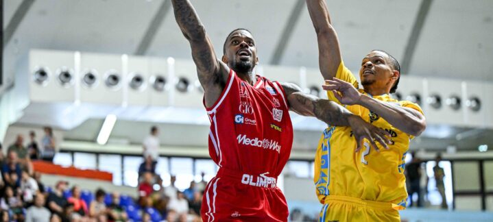 Jugadores compiten en un partido de baloncesto, uno lanza a canasta mientras es defendido.