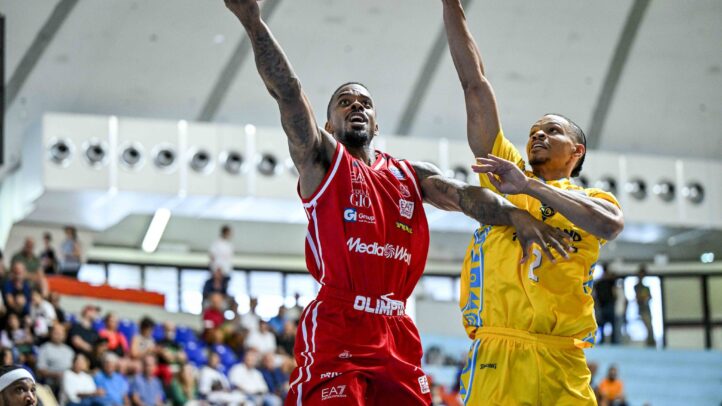 Jugadores compiten en un partido de baloncesto, uno lanza a canasta mientras es defendido.