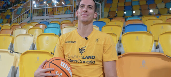 Miquel Salvó posando con un balón de baloncesto en un estadio con gradas vacías.