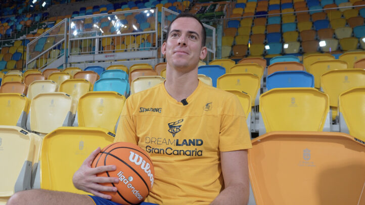 Miquel Salvó posando con un balón de baloncesto en un estadio con gradas vacías.