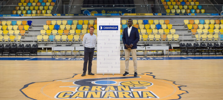 Dos personas posan junto a un panel de Canaragua en una cancha de baloncesto.