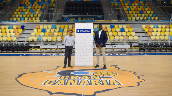 Dos personas posan junto a un panel de Canaragua en una cancha de baloncesto.