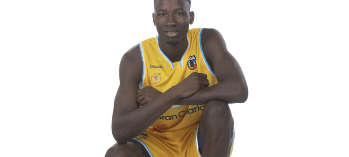 Jugando a baloncesto, un jugador posa de rodillas con un balón en la mano.