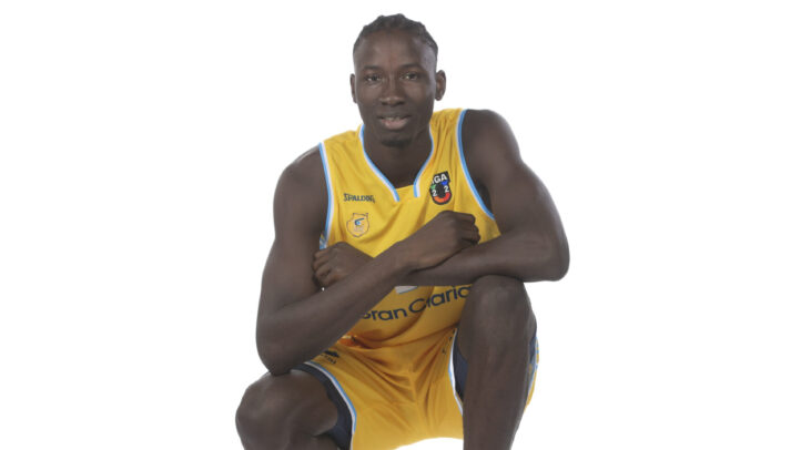 Jugando a baloncesto, un jugador posa de rodillas con un balón en la mano.