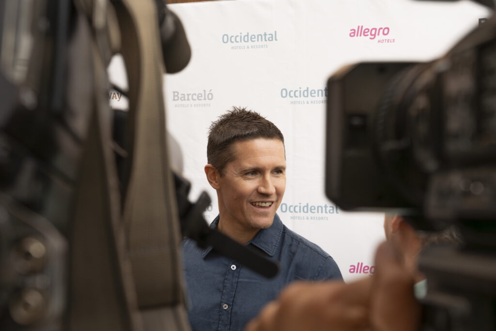 Jaka Lakovic sonriendo durante un evento, entre cámaras y un fondo promocional.