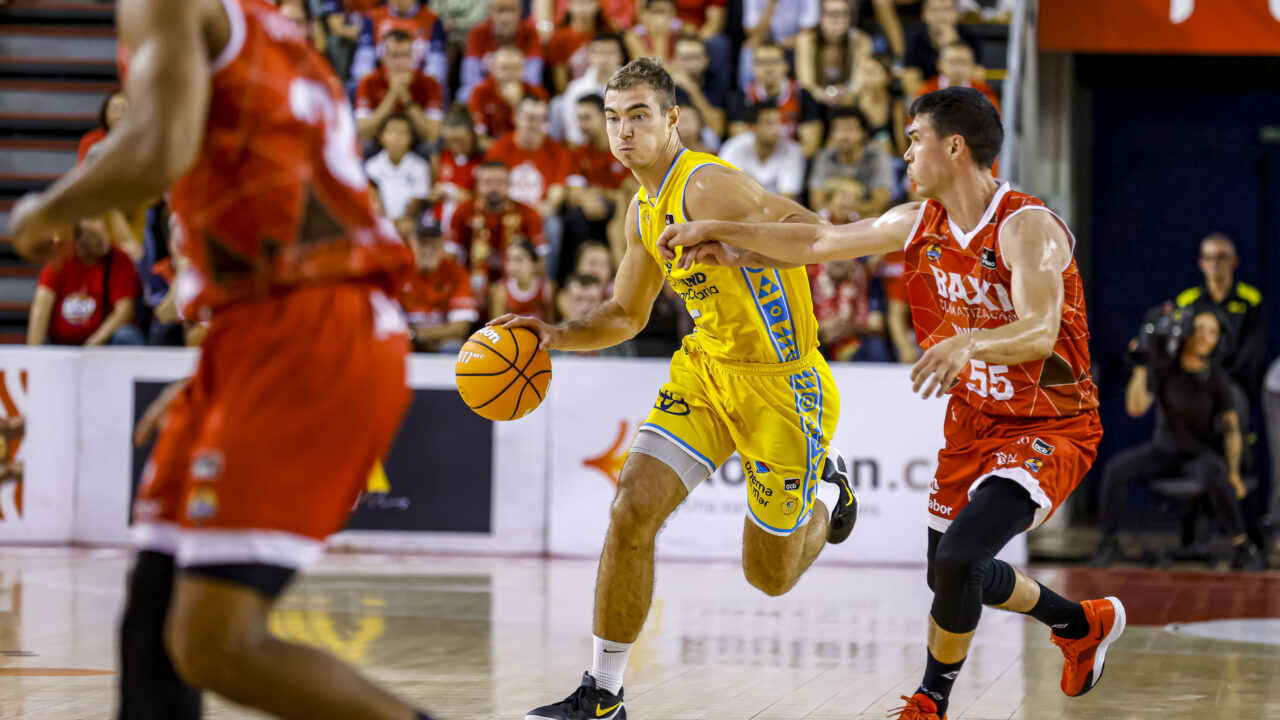 Jugadores de baloncesto compiten, uno driblando y el otro en defensa durante un partido.