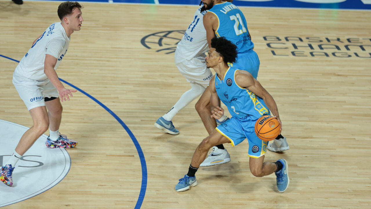 Jugadores de baloncesto en acción durante un partido, con balón en mano.