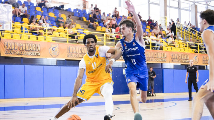 Jugadores de baloncesto compiten en la cancha, mientras uno dribla el balón.