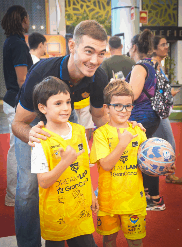 Dos niños con camisetas del Dreamland Gran Canaria posan con un jugador en un evento.